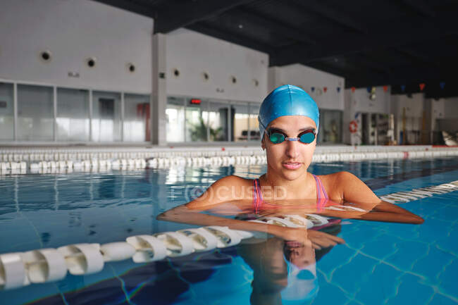 Adult sportswoman in goggles and swimwear leaning on lane line in swimming pool with transparent water and looking at camera — Stock Photo