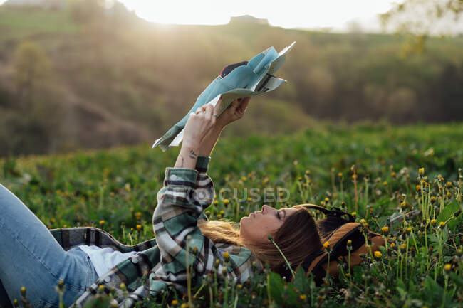 Concentrated female traveler with paper map lying on meadow against mountain in countryside — Fotografia de Stock