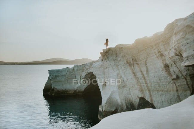 Неузнаваемый человек, стоящий на грубой скалистой скале, омытый спокойным синим морем в солнечный день в Греции — стоковое фото