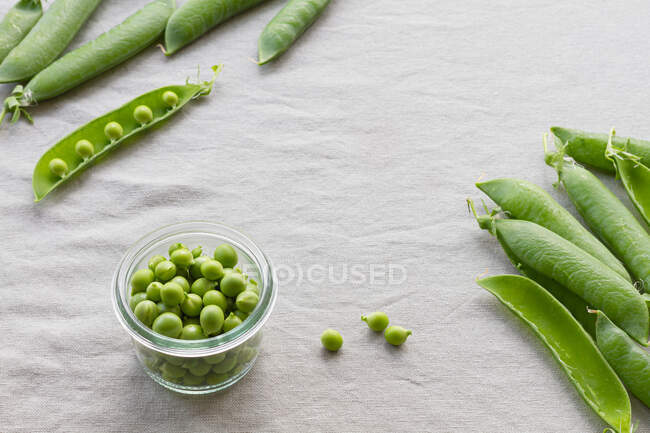 De cima de vidro tigela pequena com ervilhas verdes crocantes perto de pilha de vagens de ervilha crocante na mesa em casa — Fotografia de Stock
