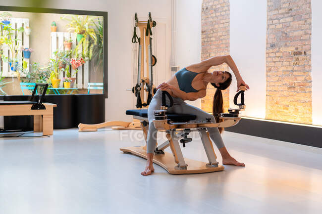 Femmina in forma focalizzata seduta su panca e braccia tese sulla macchina pilates durante l'allenamento — Foto stock