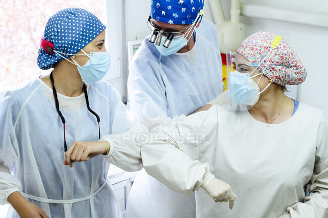 Врожай невизначений чоловічий хірург з колегами-жінками в уніформі вітаючи один одного з ліктем на роботі в лікарні — стокове фото