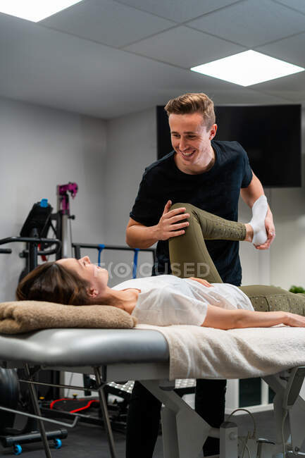 Adulto fisioterapeuta masculino tocando perna de mulher com os olhos fechados durante o exame na cama no hospital — Fotografia de Stock