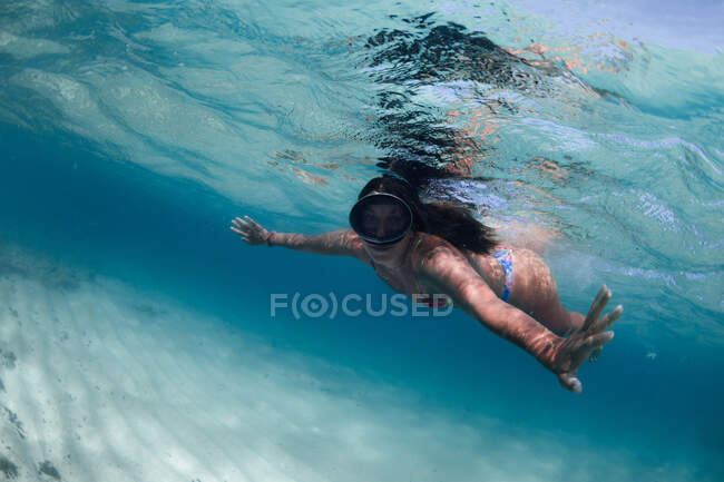 Turista donna in costume da bagno e maschera subacquea che pratica lo snorkeling mentre nuota sotto l'acqua blu dell'oceano e guarda la fotocamera — Foto stock