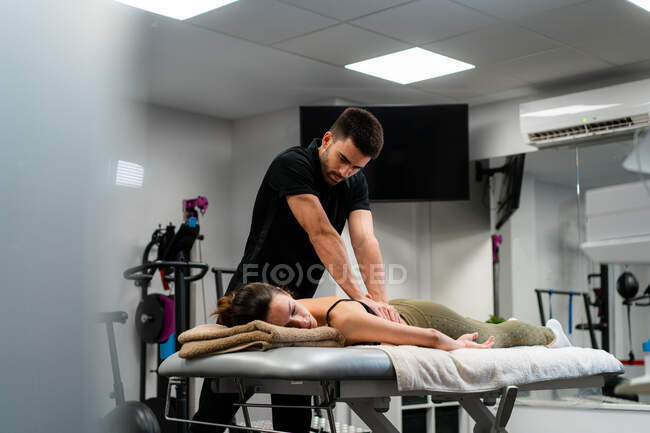 Небритый физиотерапевт-мужчина массирует спину женщины в постели во время медицинской процедуры в больнице — стоковое фото