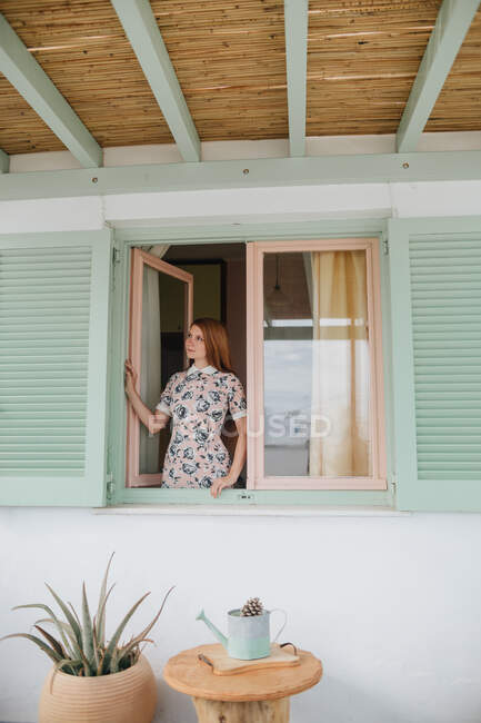 Attraktive junge Frau in Sommerkleidung steht in der Nähe ihres Hauses und schaut nach oben — Stockfoto