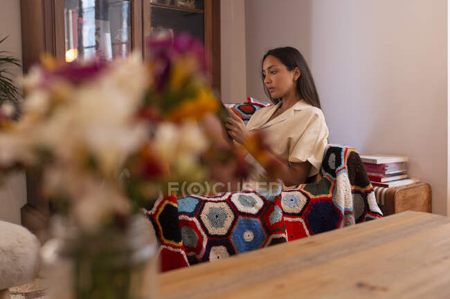 Seitenansicht einer schlanken, aufmerksamen Frau in Freizeitkleidung, die ein Buch liest, während sie sich im modernen Wohnzimmer auf einem bequemen Sessel ausruht — Stockfoto