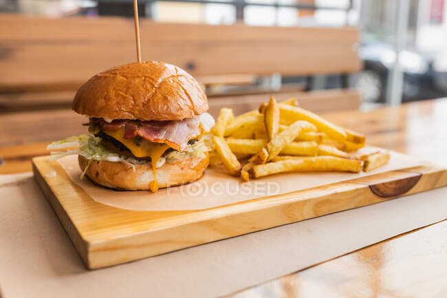 Delicious fresh hamburger and crispy French fries served on wooden board in modern fast food restaurant — Stock Photo