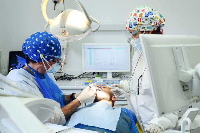 Anonymer Zahnarzt mit einem Kollegen in Uniform, der Zähne eines Patienten mit medizinischen Werkzeugen in einer modernen Klinik operiert — Stockfoto