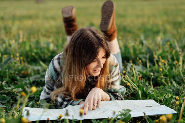 Щаслива жінка мандрівник з паперовою картою лежить на лузі в сільській місцевості — стокове фото