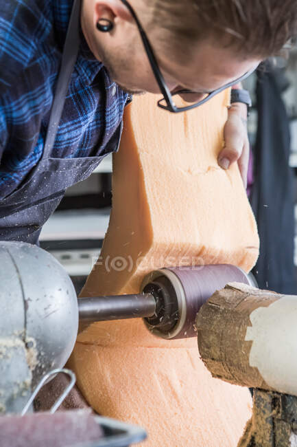 Male artisan polishing piece of foam rubber with electric grinder while making seat for motorcycle in workshop — Stock Photo