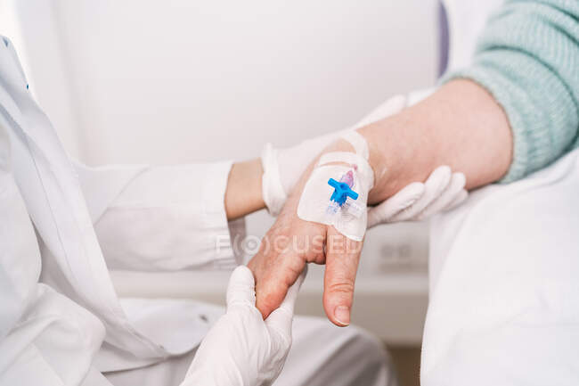Высокий угол наклона анонимного медика в одноразовых перчатках, помещающего внутривенный катетер на руку больного в больнице — стоковое фото