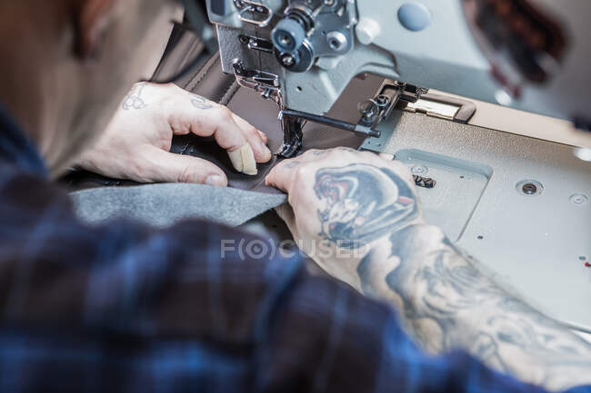 De arriba artesano masculino usando máquina de coser mientras que crea tapicería para el asiento de la motocicleta en taller - foto de stock