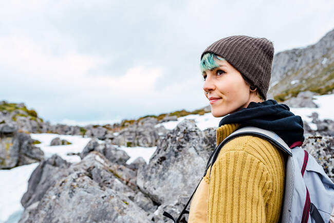 Боковой вид женщины с рюкзаком, стоящей на снежной лужайке в долине гор на вершинах Европы — стоковое фото