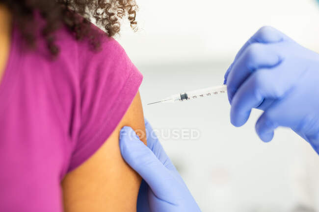 Cropped unrecognizable female medical specialist in protective uniform and latex gloves vaccinating anonymous African American female patient in clinic during coronavirus outbreak — Stock Photo