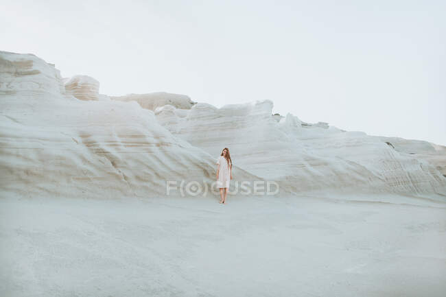 Mujer en vestido blanco paseando a lo largo de estrecho pasaje formado por rocas curvas de luz en el clima soleado en Sarakiniko Grecia - foto de stock