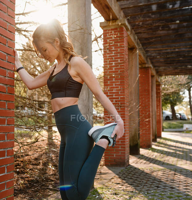 Vista laterale di giovane atleta donna in activewear guardando in basso durante l'allenamento in retroilluminazione — Foto stock