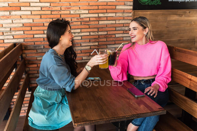 Sid vista de joven elegante hembra teniendo un refresco mientras está sentado en la mesa en una cafetería - foto de stock