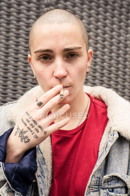 Auto confiante jovem transexual na jaqueta de ganga fumar cigarro enquanto olha para a câmera — Fotografia de Stock
