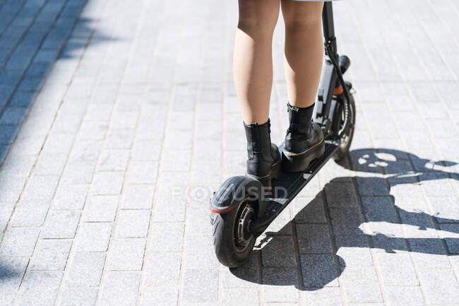 Cropped unrecognizable female in casual wear riding scooter on paved sidewalk — Foto stock
