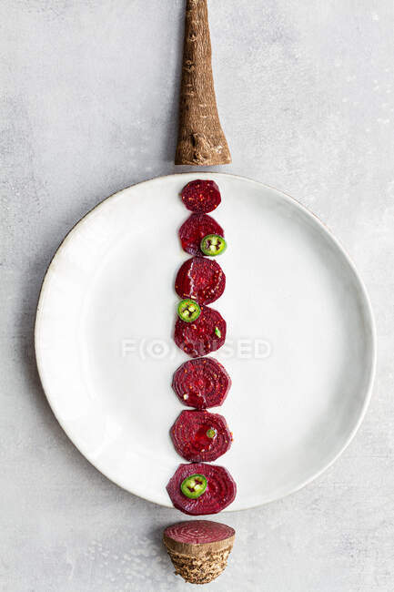 Composizione creativa aerea di fette di barbabietola dolce disposte in linea su piatto bianco con radice vegetale e coda sui lati — Foto stock