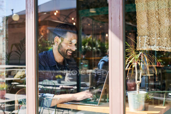 Grâce à la vue en verre de l'adulte ethnique masculin employé à distance travaillant sur netbook à la table — Photo de stock