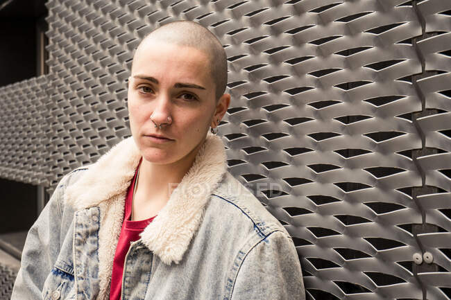 Transgender-Person in Jeansjacke mit Pelz und Ohrringen blickt bei Tageslicht in die Kamera — Stockfoto