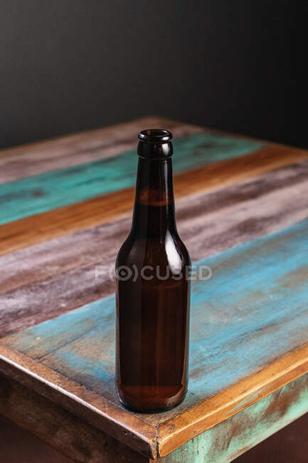 Bouteille en verre foncé de boisson alcoolisée sur une table en bois peinte en forme de carré à la maison — Photo de stock