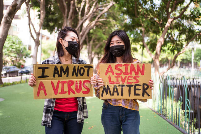 Ethnic females in masks holding posters protesting against racism in city street and looking away — Stock Photo