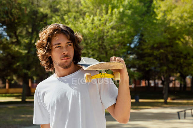 Retrato de um skatista segurando sua prancha sobre um ombro. — Fotografia de Stock