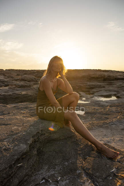Вид збоку на молоду жінку, що стоїть на скелі під час заходу сонця і дивиться вниз — стокове фото