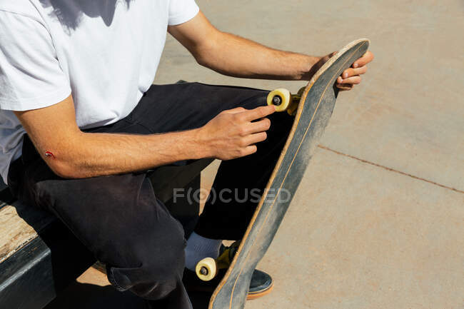 Man's hands with a scrape touching a wheel of his skateboard — Stock Photo