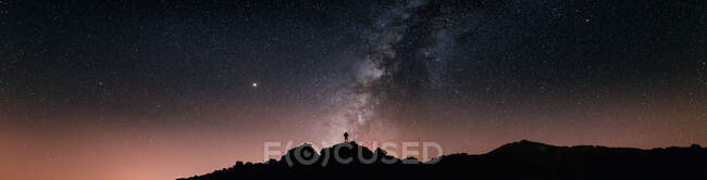 Silhouette di turista anonimo in piedi sulla scogliera contro il cielo stellato incandescente di notte — Foto stock