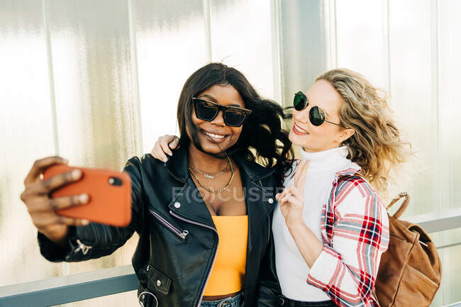 Zufriedene multiethnische Freundinnen, die am Wochenende auf der Straße stehen und Selbstaufnahmen mit dem Handy machen — Stockfoto