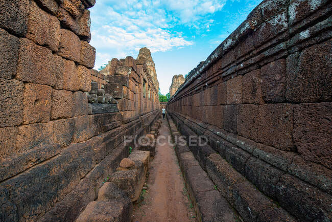 Turista feminina anônimo em passarela estreita entre paredes de alvenaria envelhecidas do complexo do templo no Camboja sob céu azul nublado — Fotografia de Stock