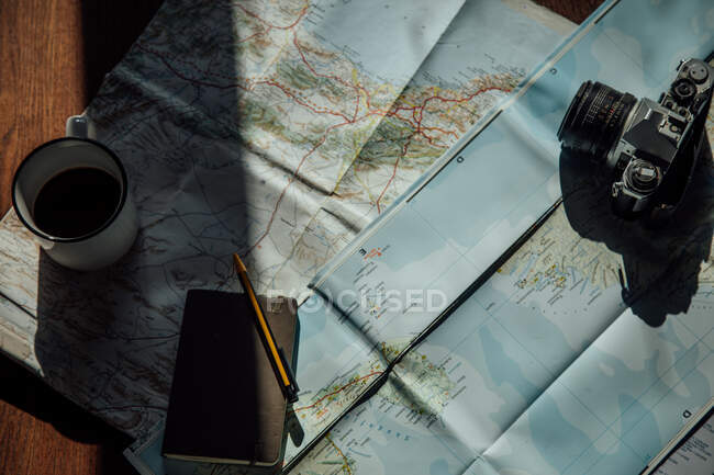 Top view of vintage photo camera and metal mug of coffee on route map during trip - foto de stock