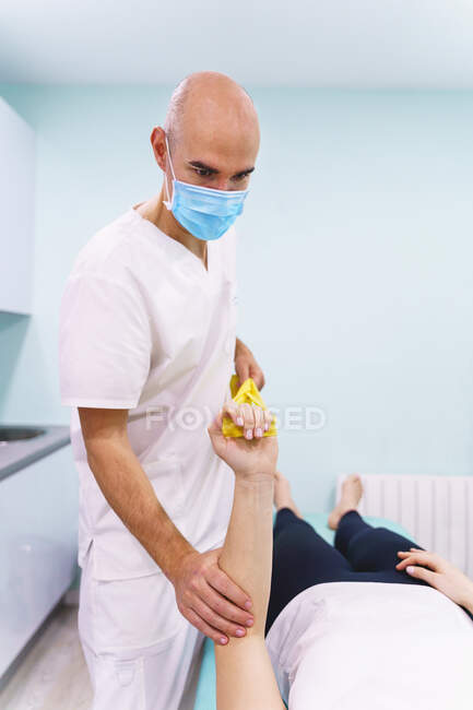 Чоловічий лікар у стерильній масці з еластичною смужкою допомагає жінці, яка не розпізнає врожай, під час одужання в лікарні. — стокове фото