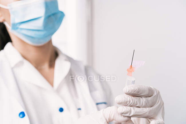 Обрізана невизначена жінка-лікар в захисній масці і з вакциною від коронавірусу в шприці, що стоїть в яскравій медичній кімнаті лікарні — стокове фото