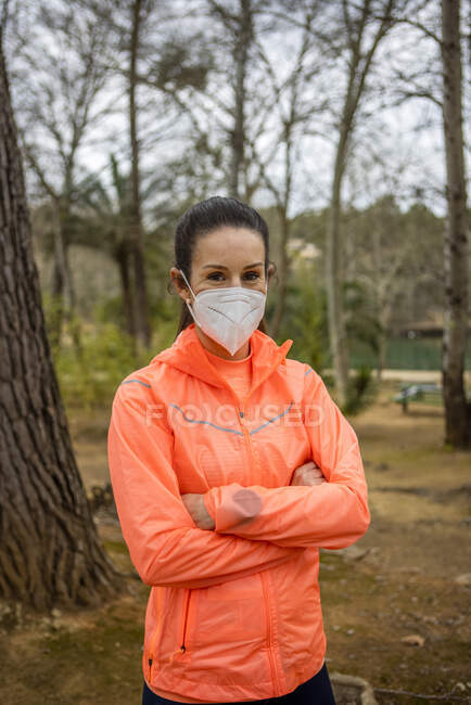 Сама впевнена жінка в захисній масці з схрещеними руками дивиться на камеру під час пандемії COVID 19 на відкритому повітрі — стокове фото
