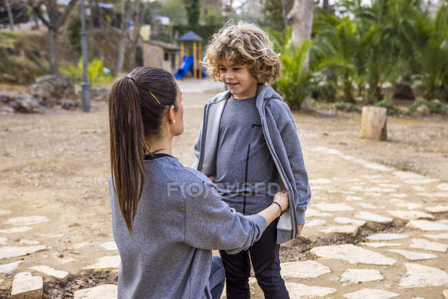 Side view of mom with boy in casual apparel standing on nature while looking at each other - foto de stock