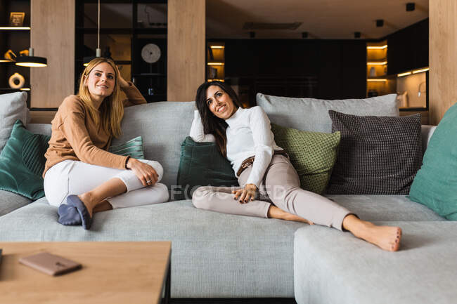 Lächelnde lesbische Frauen sitzen auf der Couch im Wohnzimmer und sehen interessante Filme, während sie das Wochenende zusammen genießen — Stockfoto