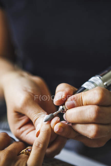 From above of crop unrecognizable female master using electric nail file while doing manicure for client in beauty salon — Stock Photo