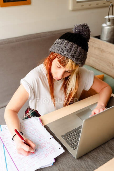 Desde arriba viajera femenina enfocada sentada en la mesa en camión y tomando notas mientras trabaja en el proyecto remotamente - foto de stock
