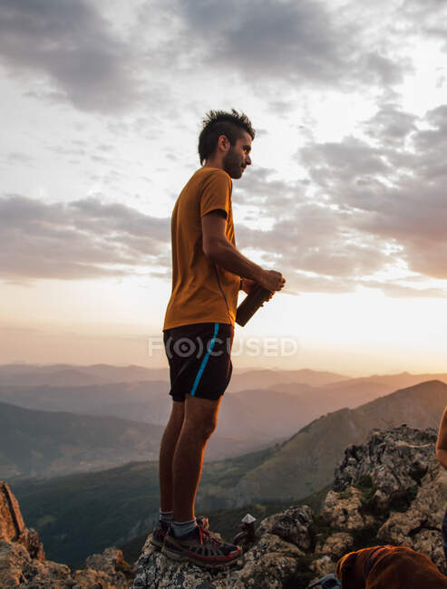 L'uomo in piedi sulla cima del masso che riposa acqua potabile sopra la valle degli altopiani sotto il cielo del tramonto — Foto stock