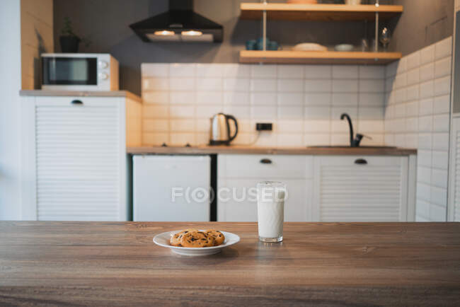 Тарілка зі смачним вівсяним печивом з шоколадними чіпсами проти склянки молока на дерев'яному столі — стокове фото