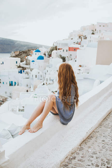 Rückansicht einer unkenntlichen Reisenden, die das Dorf Oia auf Santorin an einem windigen Tag in Griechenland bewundert — Stockfoto