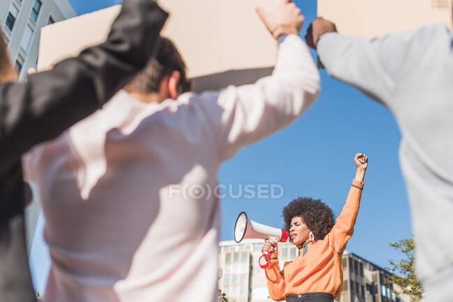 African American female social justice warrior with speaker against crop anonymous multiracial people with placards fighting for human rights in town - foto de stock