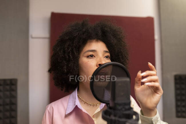 Чорна співачка співає пісню проти мікрофона з поп-фільтром, стоячи з рукою на стегні і дивлячись вперед в звуковій студії — стокове фото
