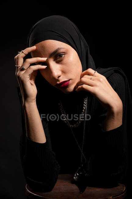 Приваблива молода ісламська жінка в чорному одязі і хіджаб торкається обличчя м'яко з закритими очима — стокове фото