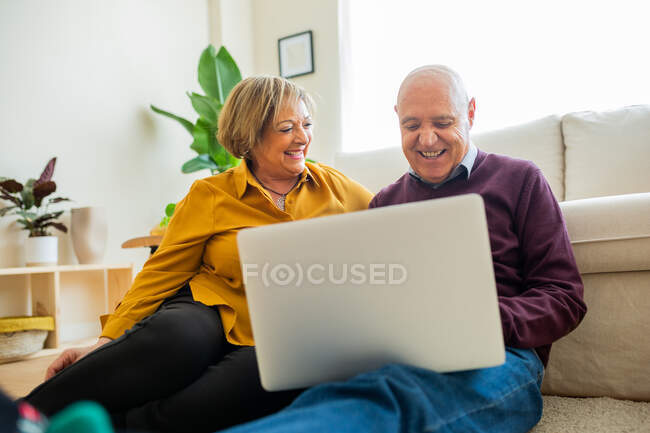 Alegre pareja madura hablando en video chat en el ordenador portátil en la sala de estar - foto de stock